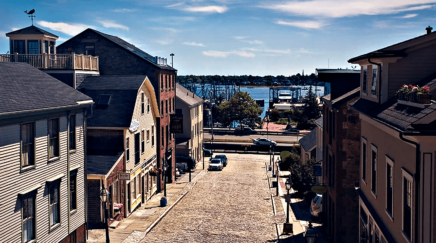 Cobblestone Centre Street in the New Bedford Historic District, lined with whaling-era buildings and sloping down to the working harbor